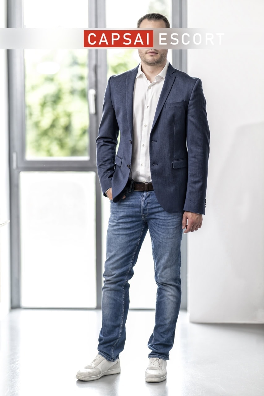 Callboy Noah aus Essen im dunkelblauen Sakko vor einem großen Fenster